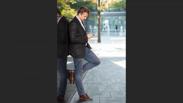 Elegant man leans against a wall and look at the phone