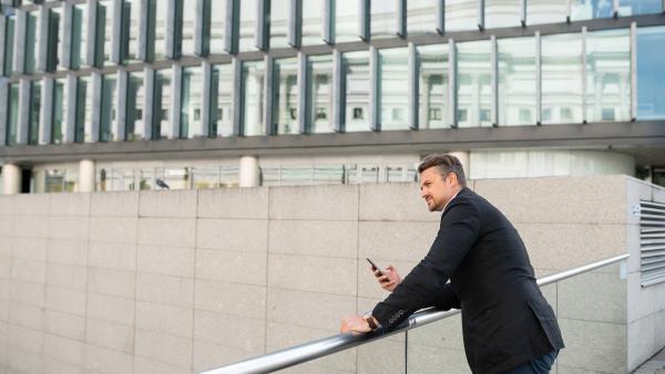 Man standing with phone in front off glass and concrete surface