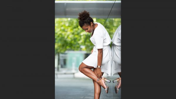 Woman leans on wall and put on a shoe