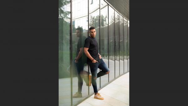 Young adult man leans on glass wall